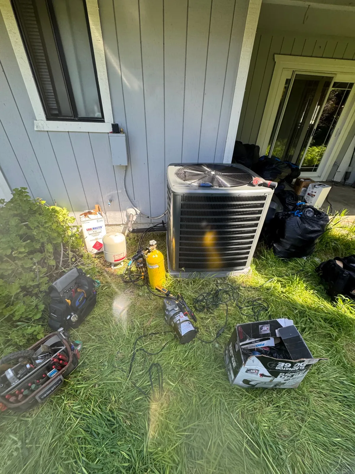 Refrigerant gauges, nitrogen tank and vacuum pump set up beside an air conditioning condenser during a repair