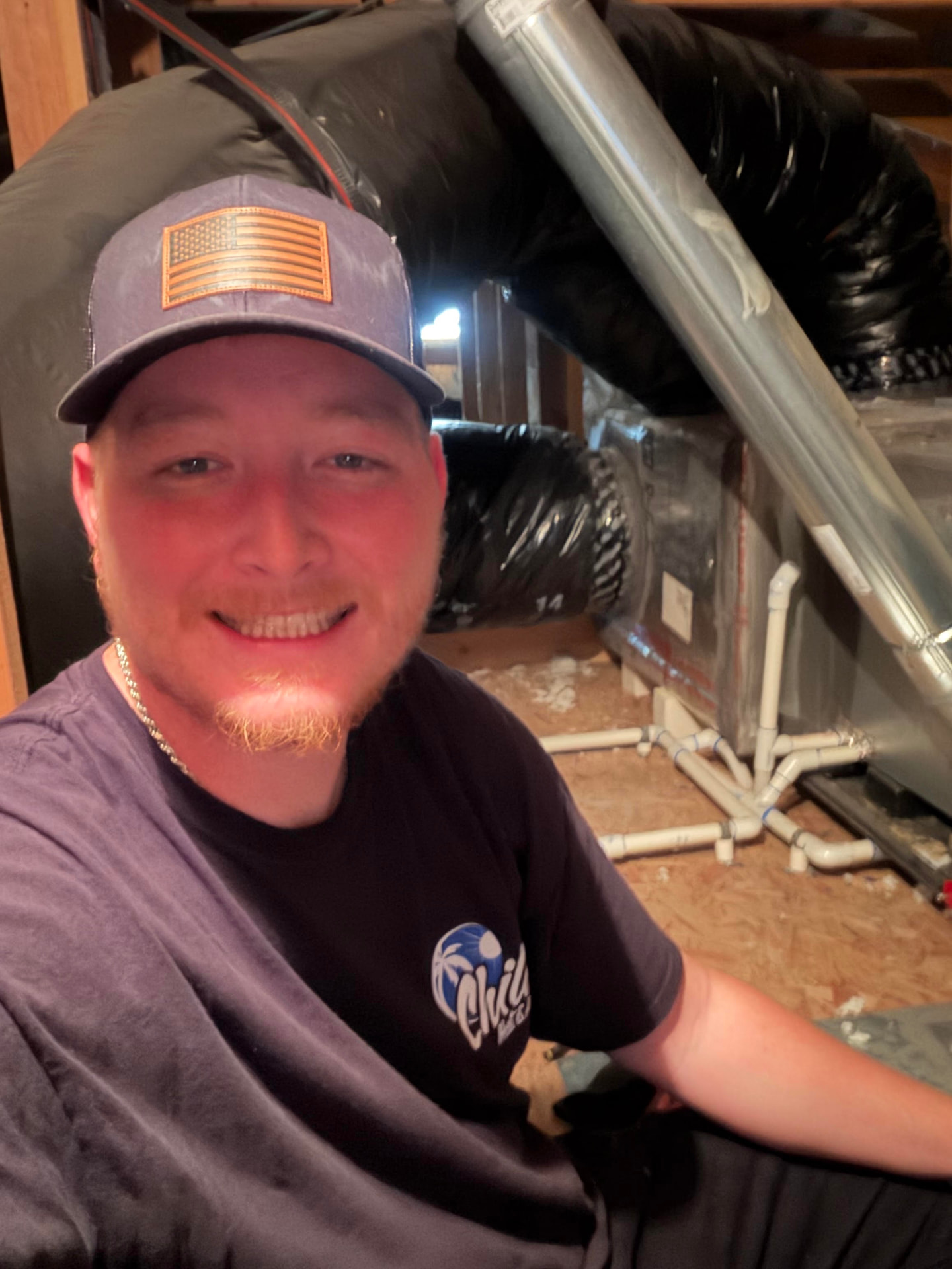 Cameron Hill, owner of Chill Heating and Air, smiling in an attic beside an air handler